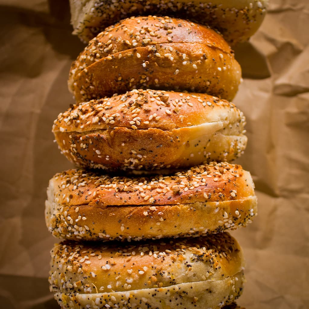 A tall stack of freshly baked sesame and poppy-seed bagels on brown paper