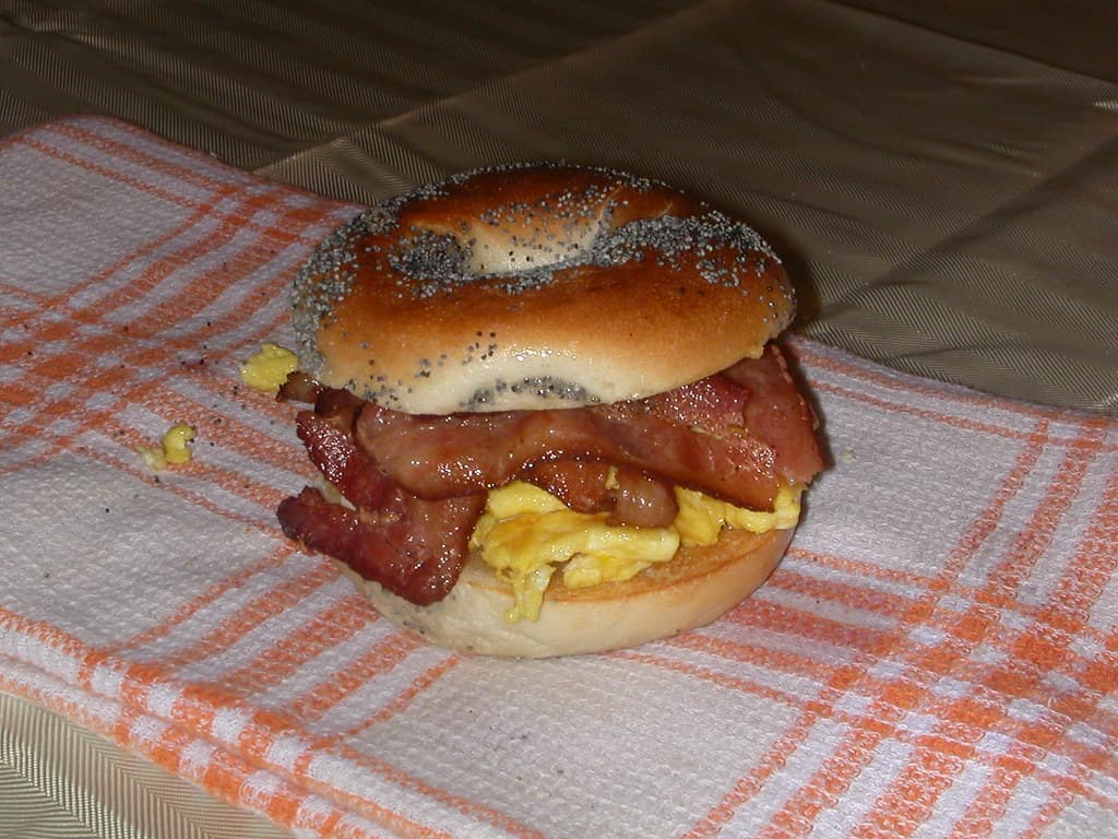 Poppy-seed breakfast bagel stacked with smoked bacon and scrambled egg