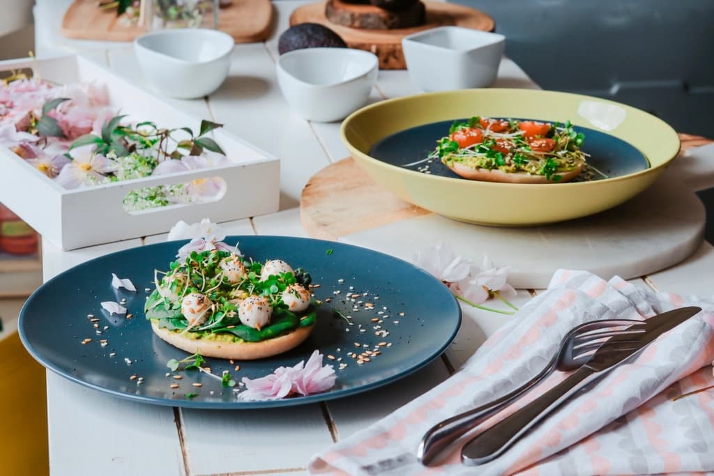 Fresh New York bagels topped with smashed avocado, microgreens, tomato and sesame, on dark plates